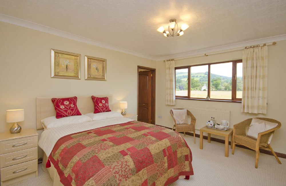 Cream painted bedroom with red bed clothes. Window with nice view out to field